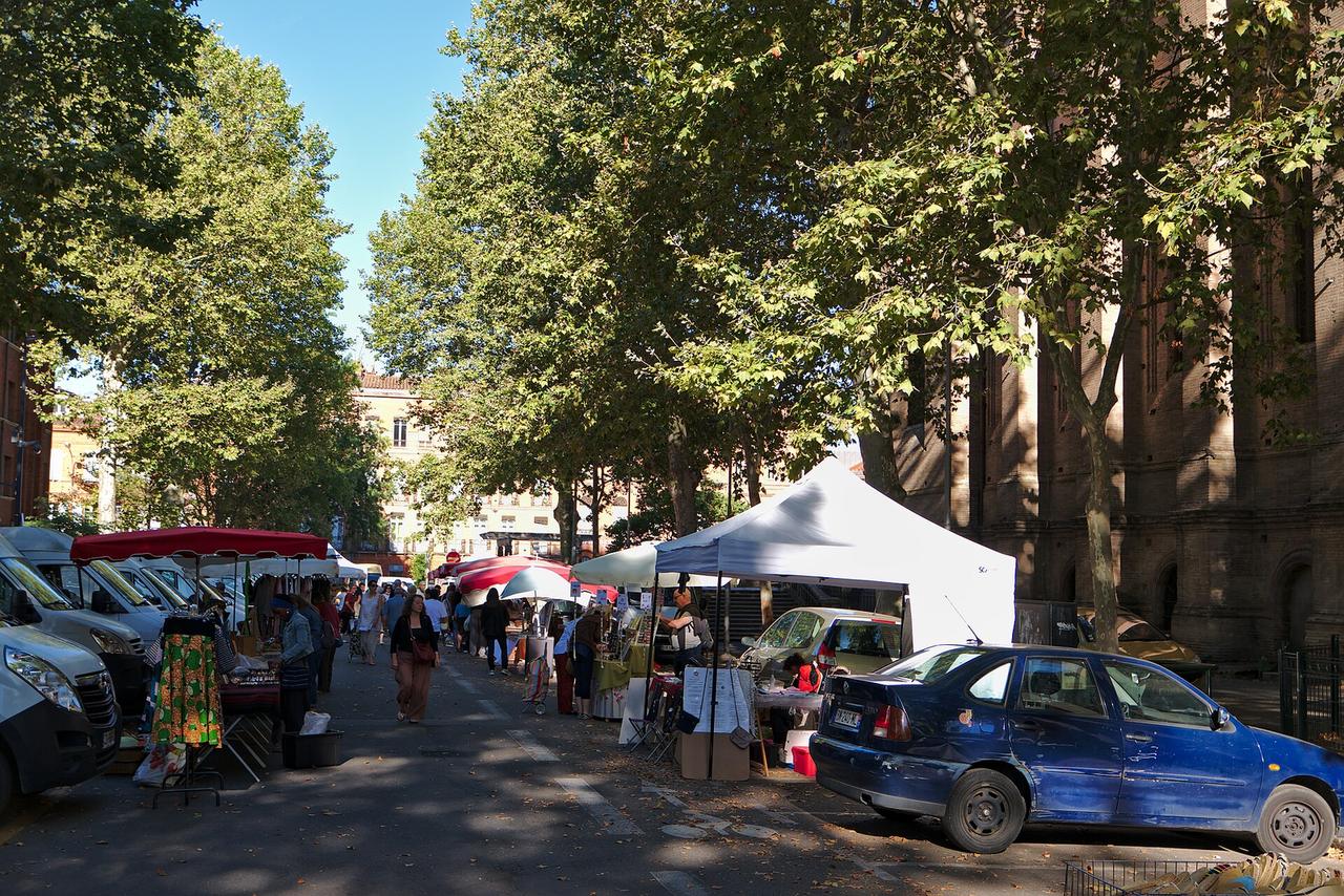 Marché de rue avec stands sous tentes et véhicules, ambiance de jour